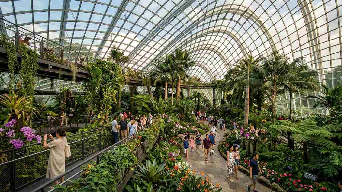 A stunning large indoor botanical garden inside a glass structure with tropical plants, tall trees, and colorful flowers from around the world. 