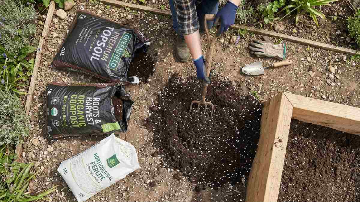 Topsoil compost and perlite bags beside a raised bed with a gardener mixing ingredients showing the best soil mix for beginner raised bed gardening. 